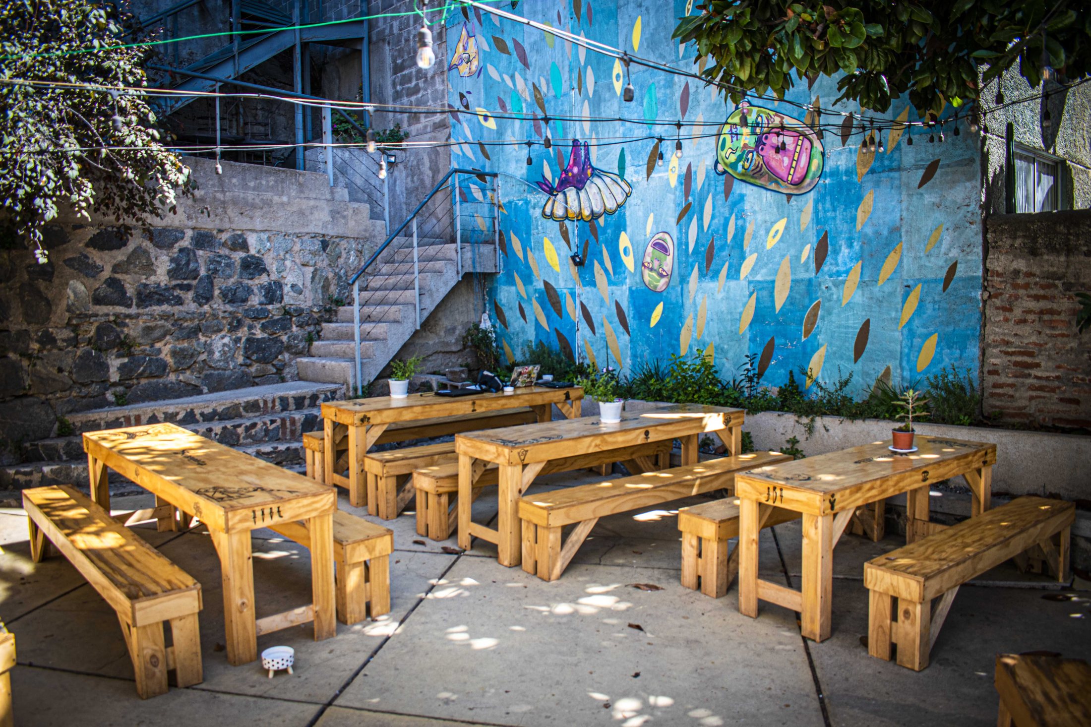 Patio cálido de Hotzenplotz con mesas de madera y mural porteño